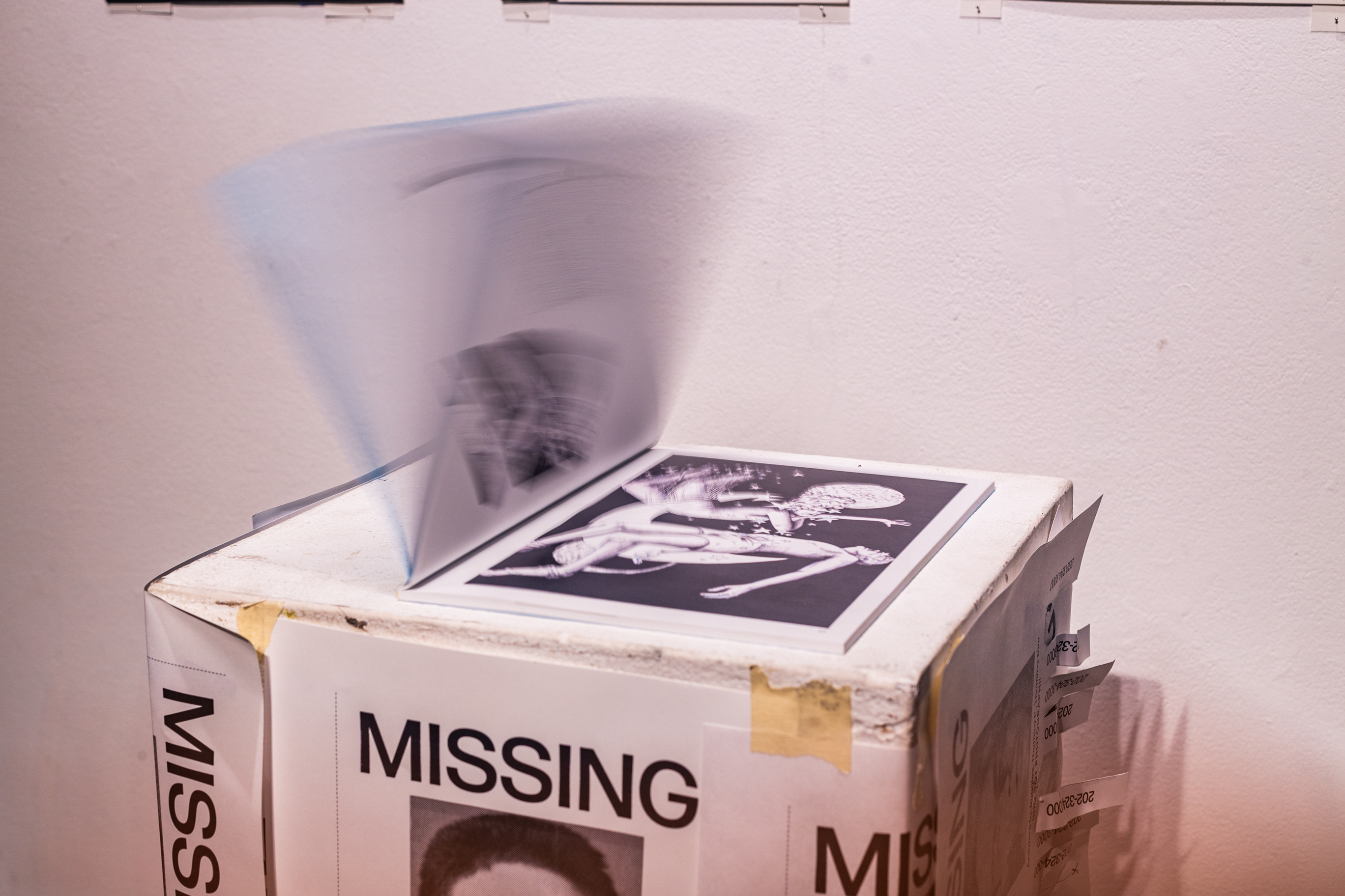 A podium with multiple fabricated missing person posters. On the podium is a book with pages being flipped through it.